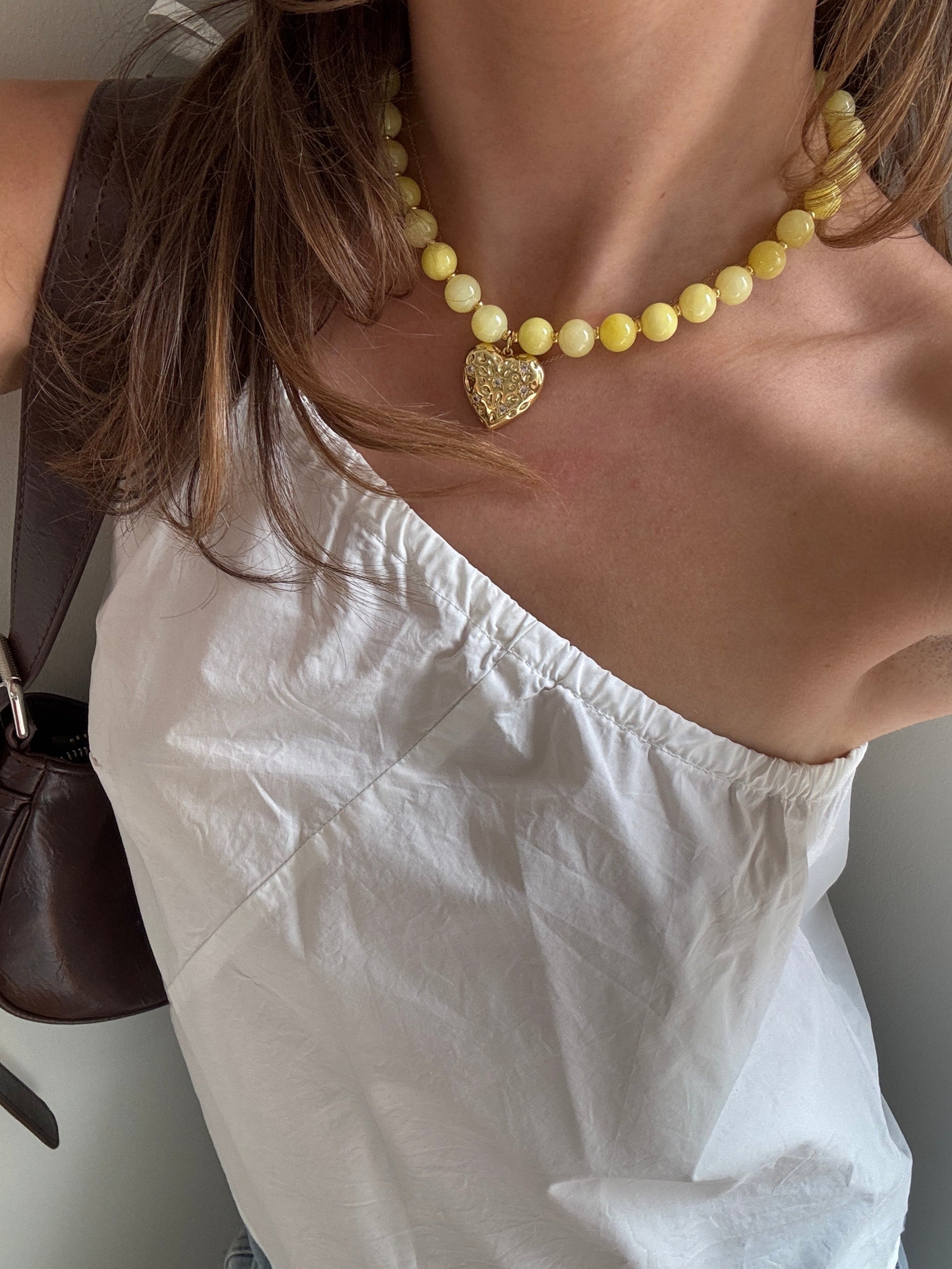Person wearing a yellow beaded necklace with a heart charm 